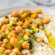 Hummus in a bowl topped with olive oil, chickpeas, chopped pickles, and spices with the text dill pickle hummus.