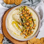 Hummus in a bowl topped with olive oil, chickpeas, chopped pickles, and spices with the text dill pickle hummus.