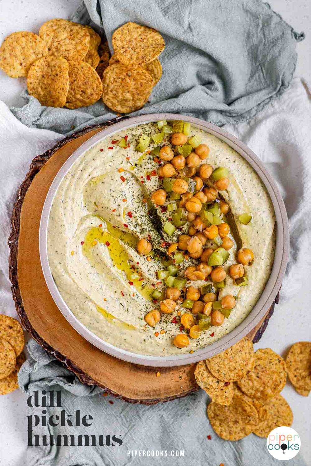 Hummus in a bowl topped with olive oil, chickpeas, chopped pickles, and spices with the text dill pickle hummus.