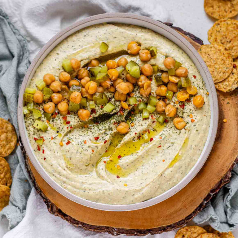 Hummus in a bowl topped with olive oil, chickpeas, chopped pickles, and spices.