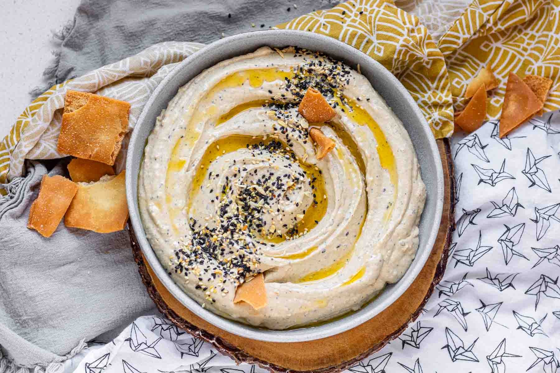 Hummus in a bowl topped with olive oil, a few pita chips, and spices.