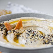 Hummus in a bowl topped with olive oil, a few pita chips, and spices.