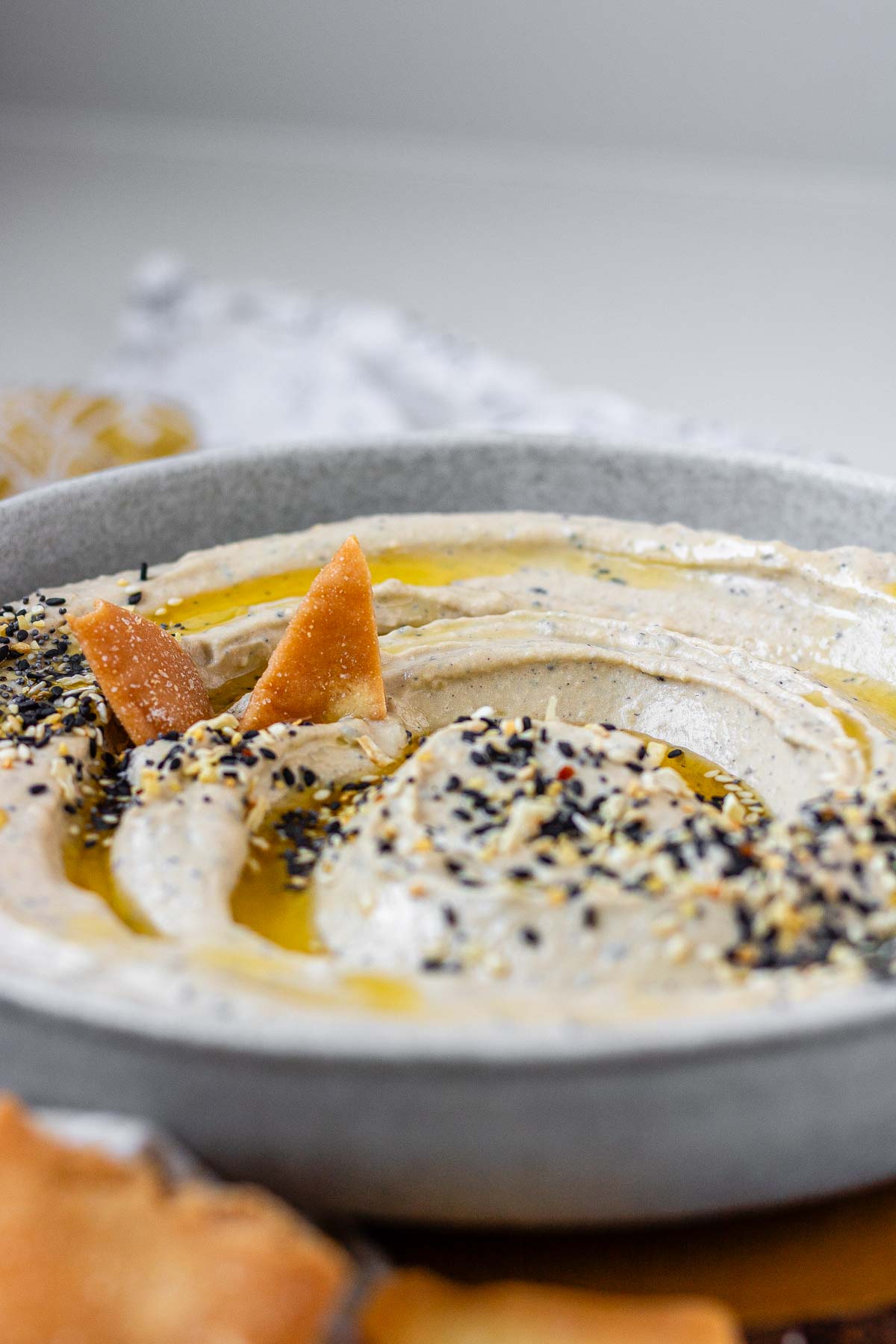 Hummus in a bowl topped with olive oil, a few pita chips, and spices.