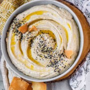 Hummus in a bowl topped with olive oil, a few pita chips, and spices.