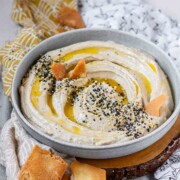 Hummus in a bowl topped with olive oil, a few pita chips, and spices.