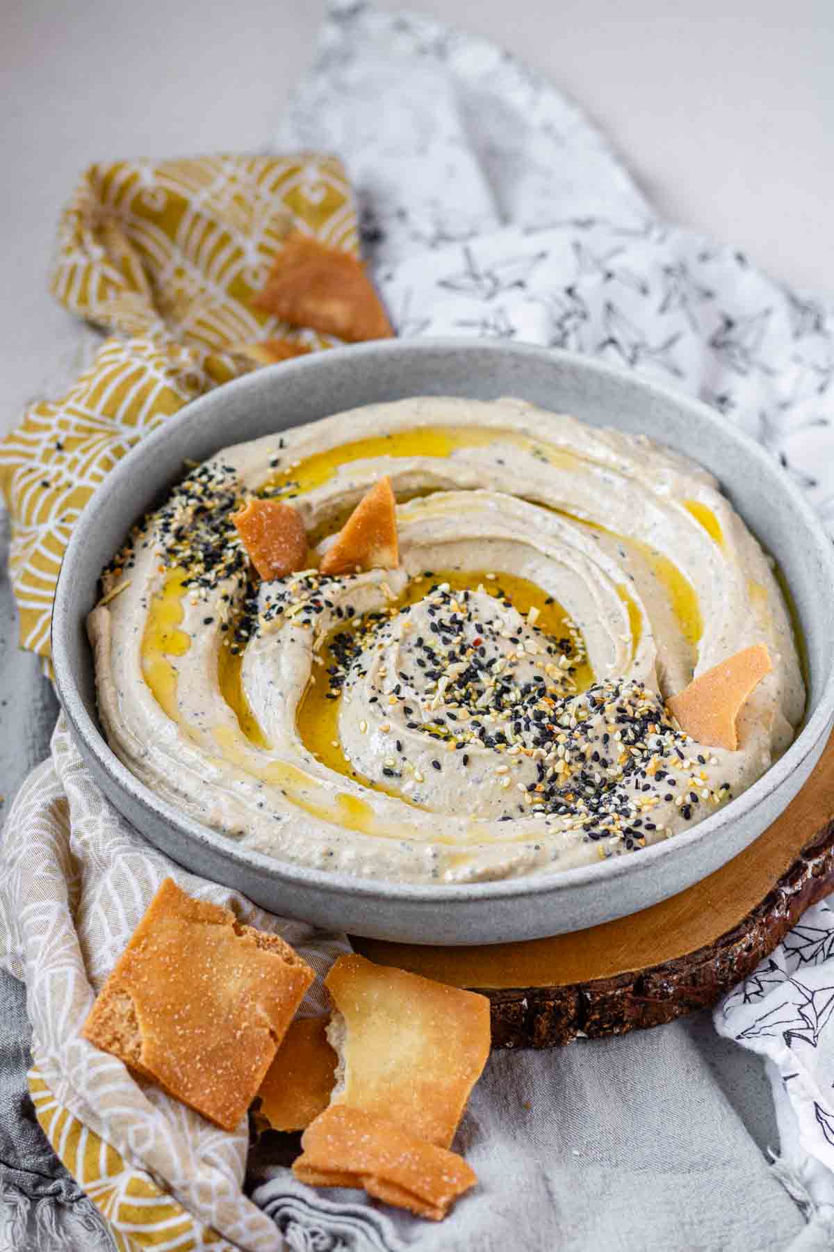 Hummus in a bowl topped with olive oil, a few pita chips, and spices.