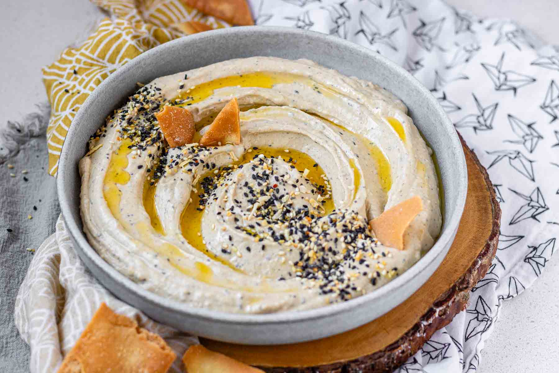Hummus in a bowl topped with olive oil, a few pita chips, and spices.