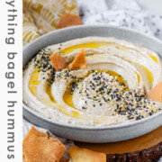 Hummus in a bowl topped with olive oil, a few pita chips, and spices with the text everything bagel hummus.