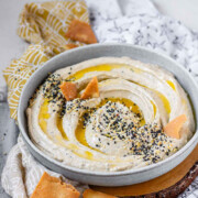 Hummus in a bowl topped with olive oil, a few pita chips, and spices with the text everything bagel hummus.