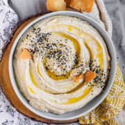 Hummus in a bowl topped with olive oil, a few pita chips, and spices with the text everything bagel hummus.