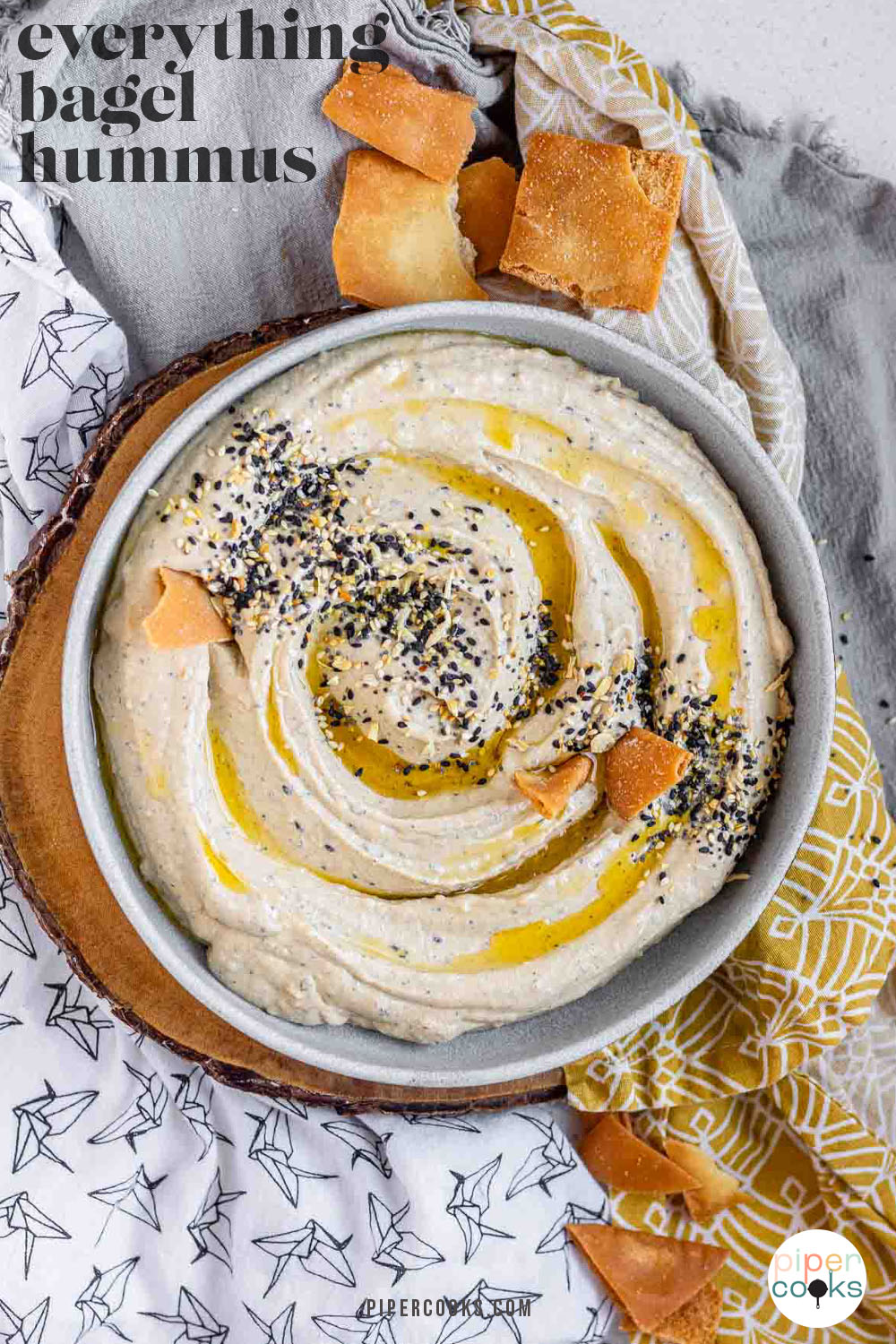 Hummus in a bowl topped with olive oil, a few pita chips, and spices with the text everything bagel hummus.