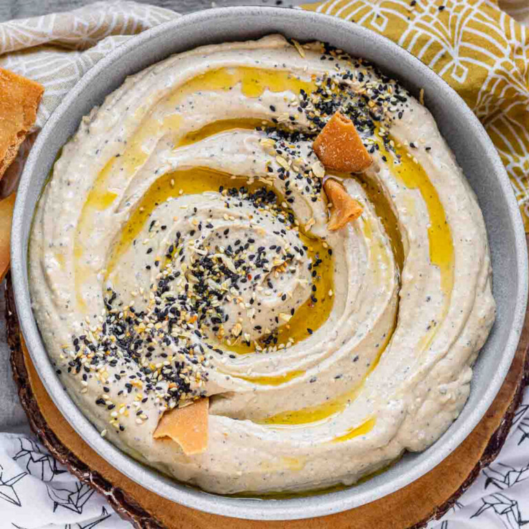 Hummus in a bowl topped with olive oil, a few pita chips, and spices.