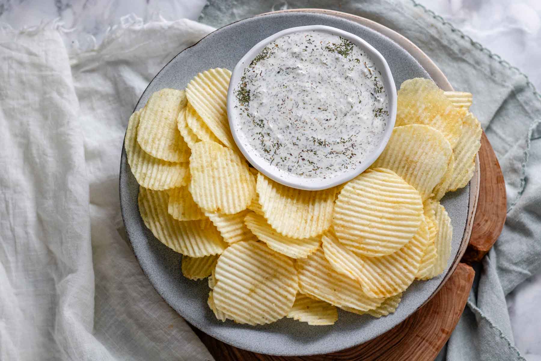 An herby dip in a bowl on a plate with chips.