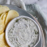 An herby dip in a bowl on a plate with chips.