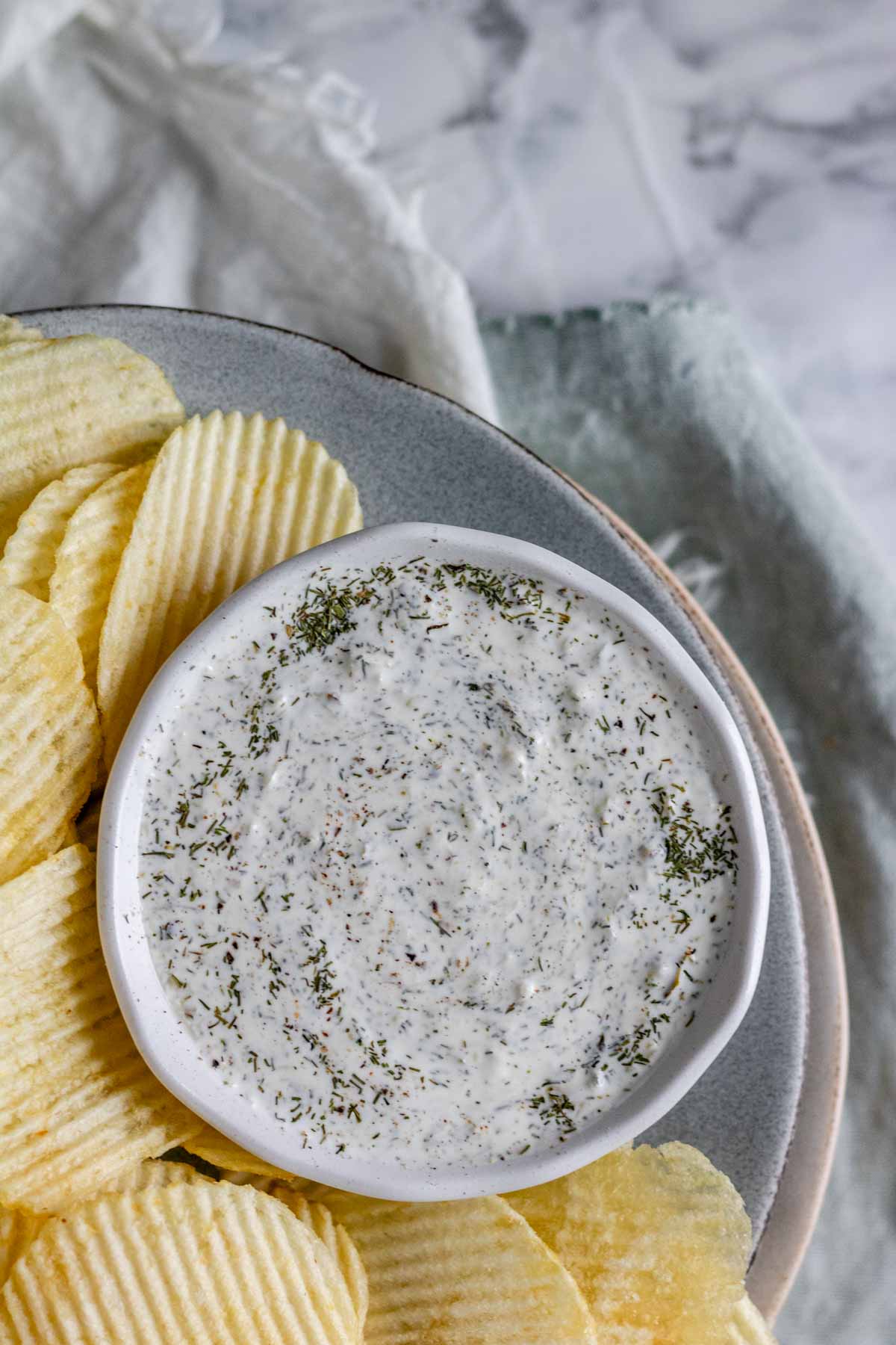 An herby dip in a bowl on a plate with chips.
