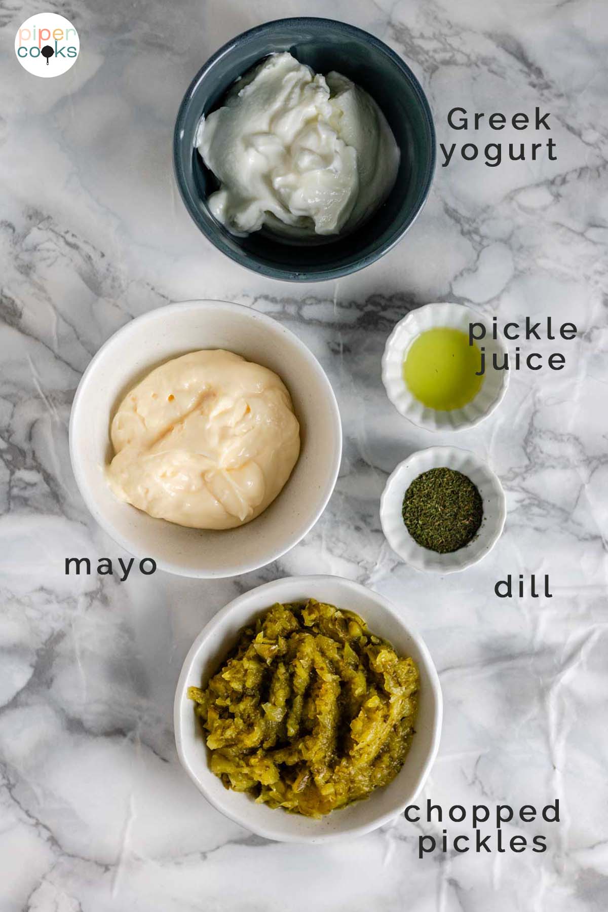 Ingredients in bowls on a counter for dill pickle dip labeled Greek yogurt, pickle juice, mayo, dill, and chopped pickles.