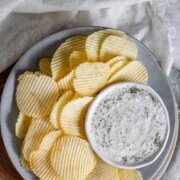 An herby dip in a bowl on a plate with chips with the text dill pickle dip.
