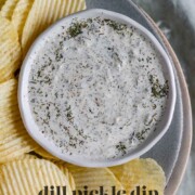 An herby dip in a bowl on a plate with chips with the text dill pickle dip.