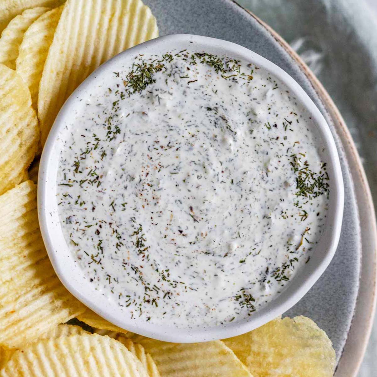 An herby dip in a bowl on a plate with chips.