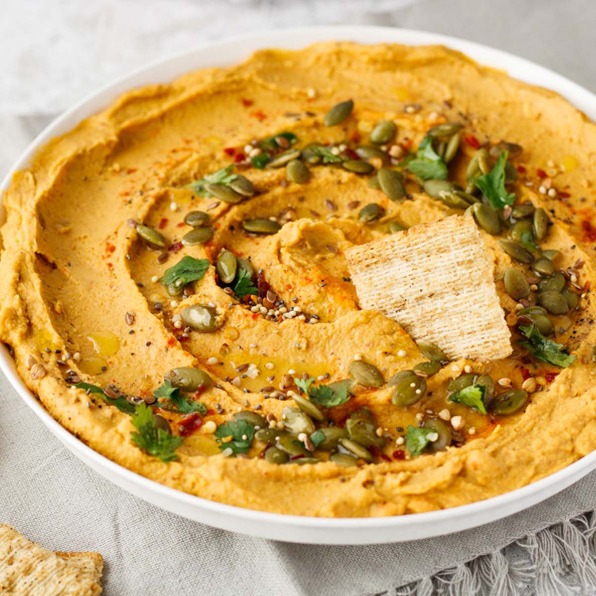 Hummus in a bowl topped with seeds and a cracker.