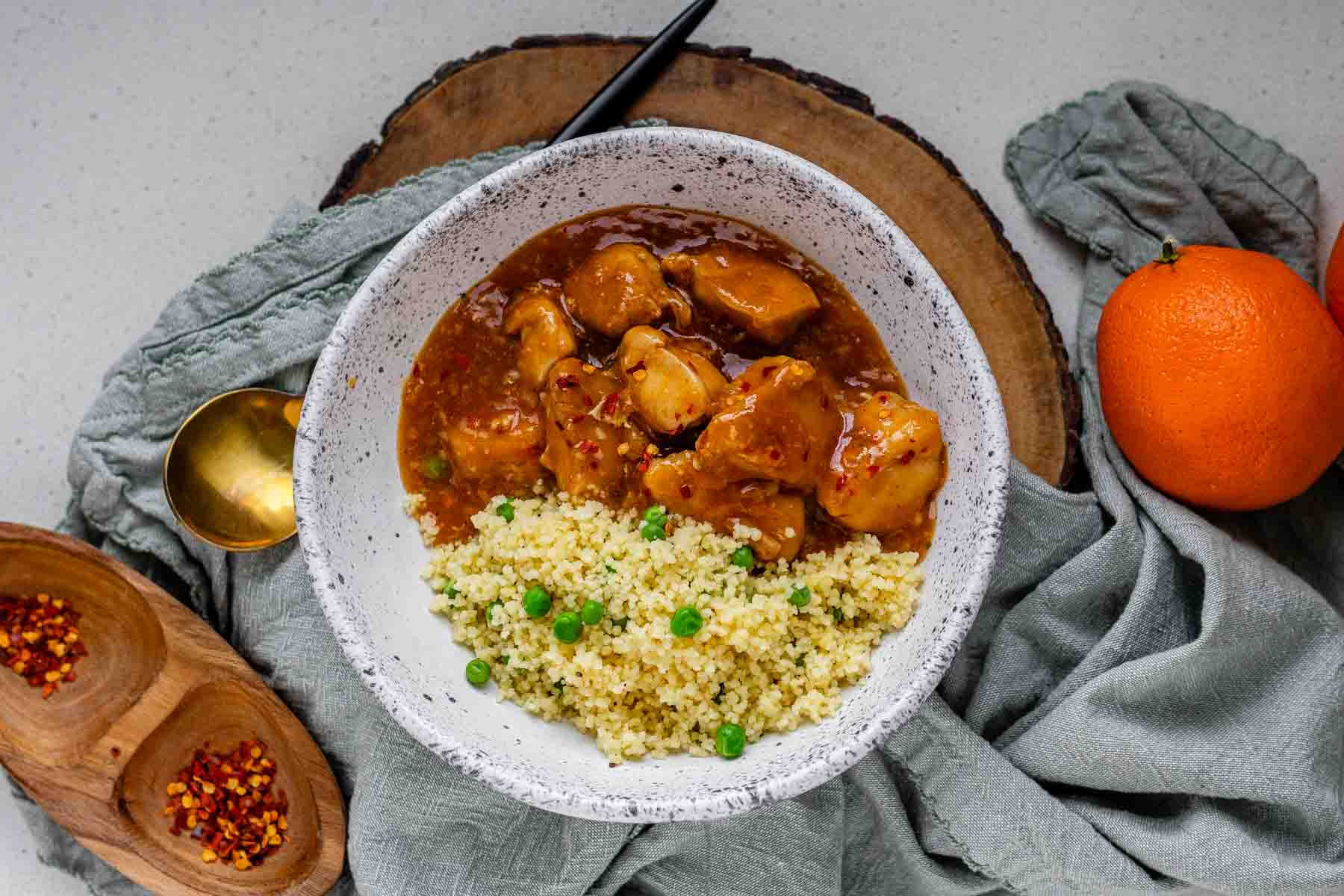 Cubed chicken in orange sauce in a bowl with couscous.