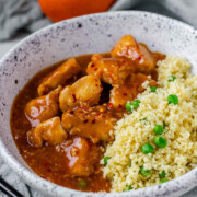 Cubed chicken in orange sauce in a bowl with couscous.