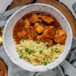 Cubed chicken in orange sauce in a bowl with couscous.
