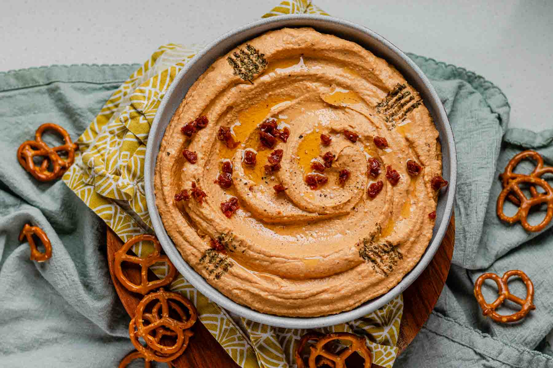 Hummus in a bowl topped with chopped sun-dried tomatoes, olive oil, and spices.