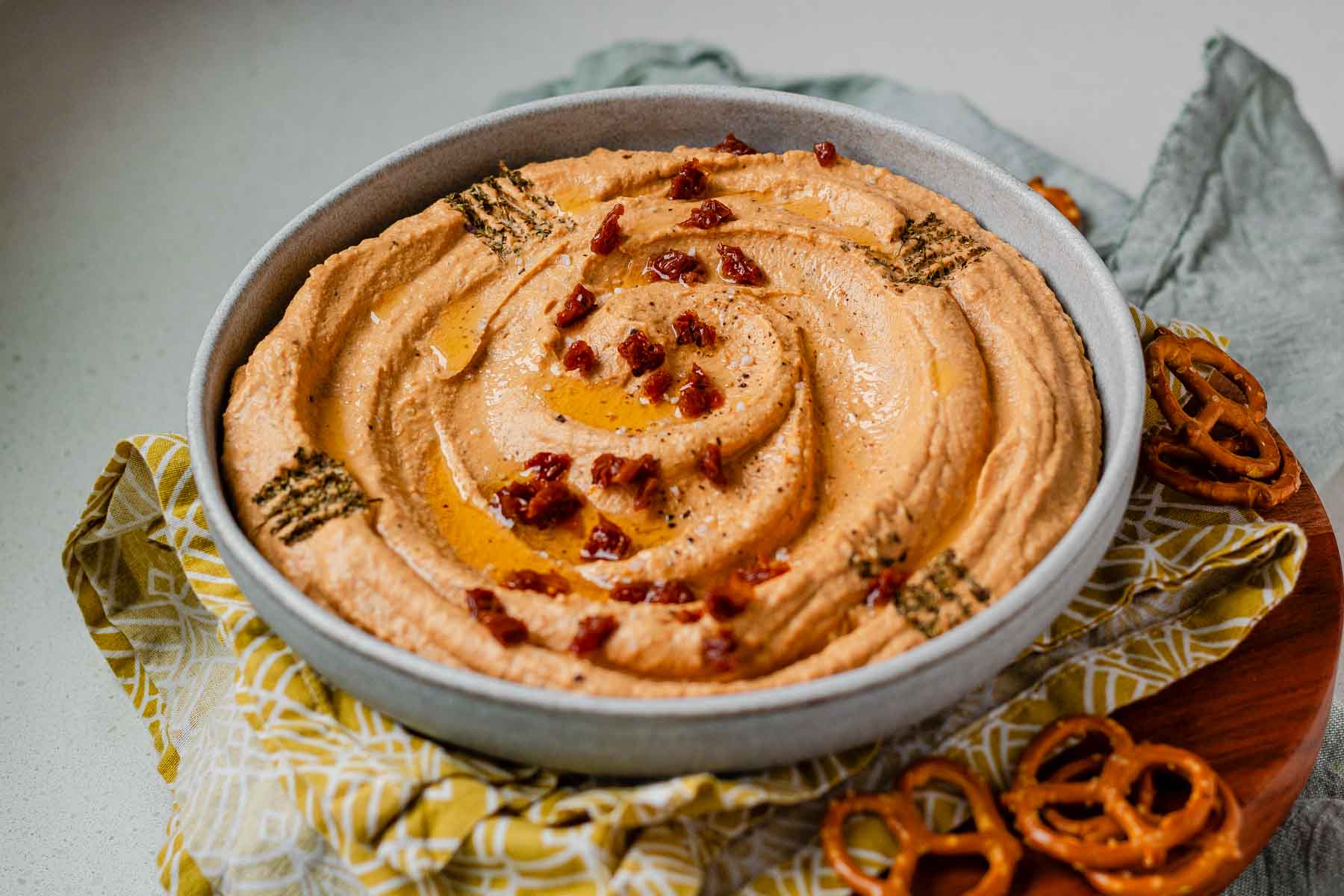Hummus in a bowl topped with chopped sun-dried tomatoes, olive oil, and spices.