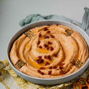 Hummus in a bowl topped with chopped sun-dried tomatoes, olive oil, and spices.