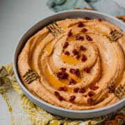 Hummus in a bowl topped with chopped sun-dried tomatoes, olive oil, and spices.