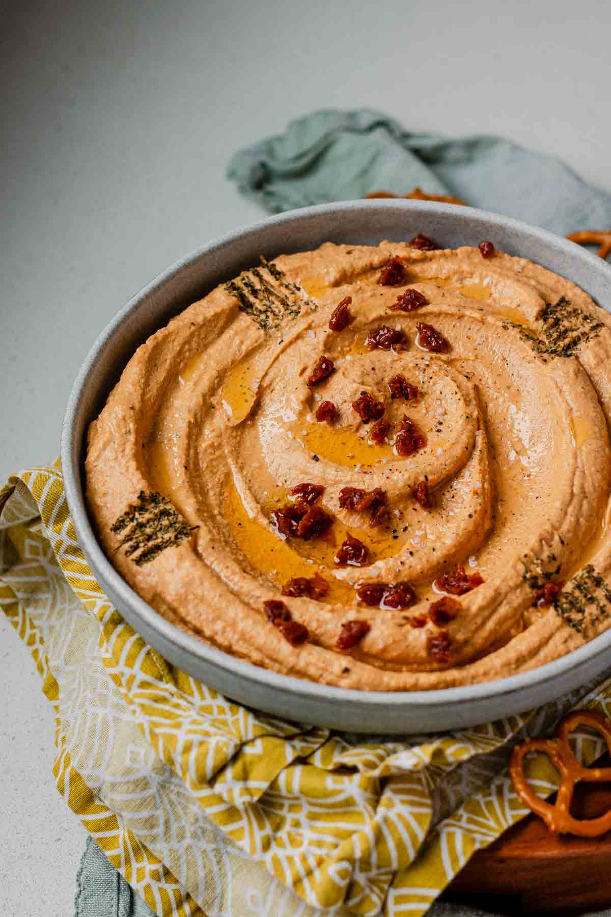 Hummus in a bowl topped with chopped sun-dried tomatoes, olive oil, and spices.