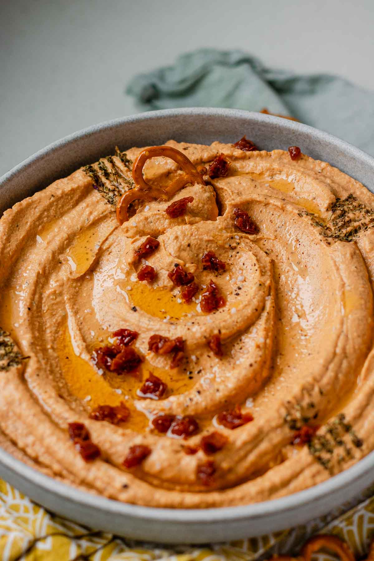 Hummus in a bowl topped with chopped sun-dried tomatoes, olive oil, and spices.