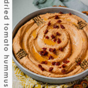 Hummus in a bowl topped with chopped sun-dried tomatoes, olive oil, and spices with the text sun-dried tomato hummus.