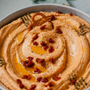 Hummus in a bowl topped with chopped sun-dried tomatoes, olive oil, and spices with the text sun-dried tomato hummus.