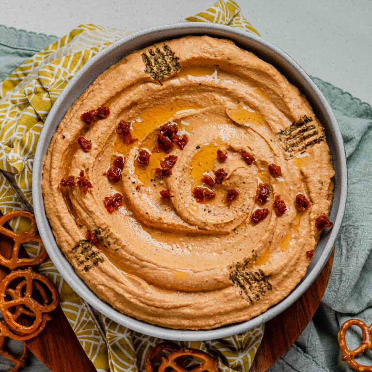 Hummus in a bowl topped with chopped sun-dried tomatoes, olive oil, and spices.