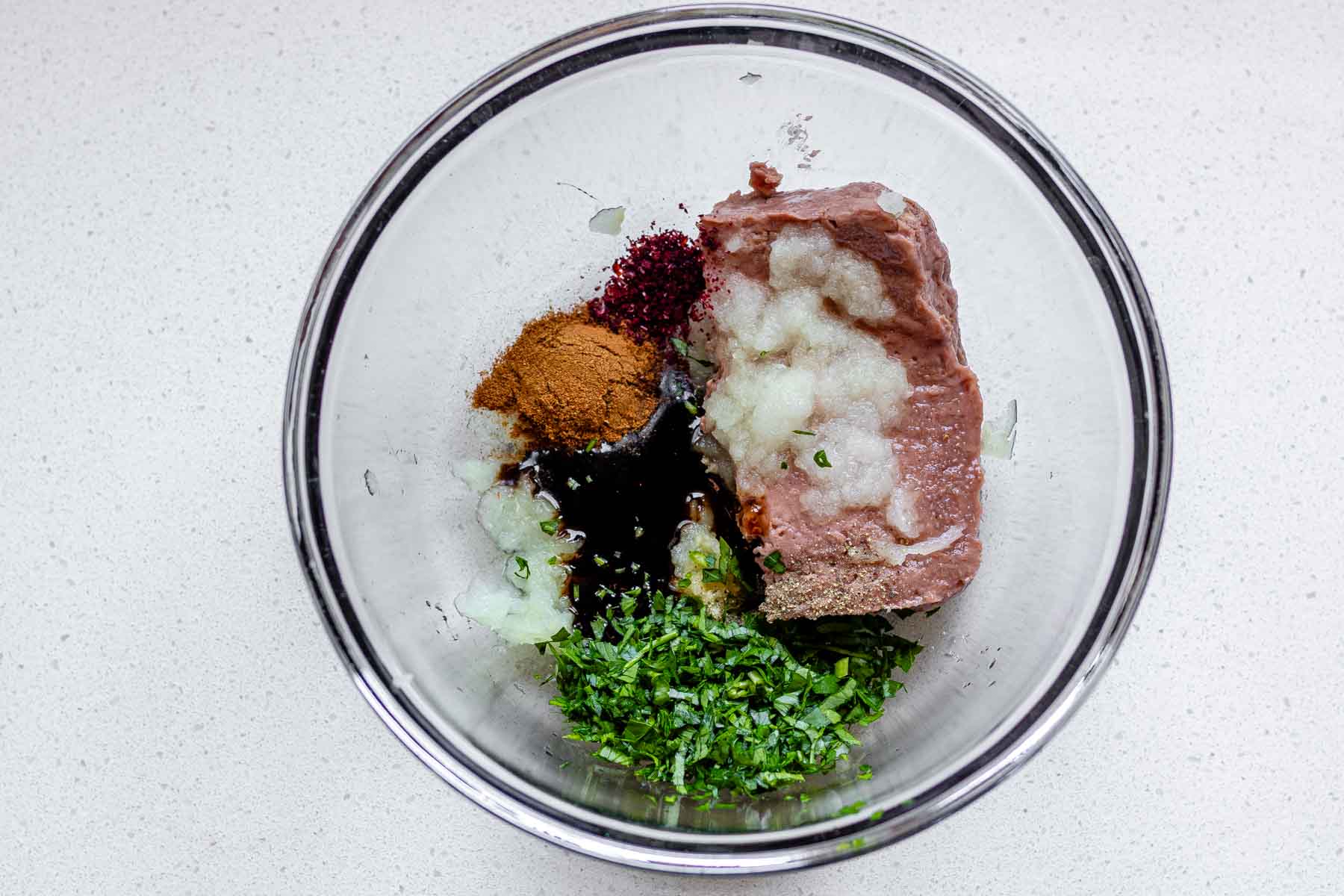A bowl with raw meat, spices, and herbs.