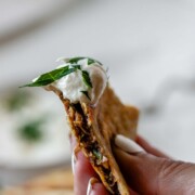 Close-up of a meat-filled fried pita with white sauce.