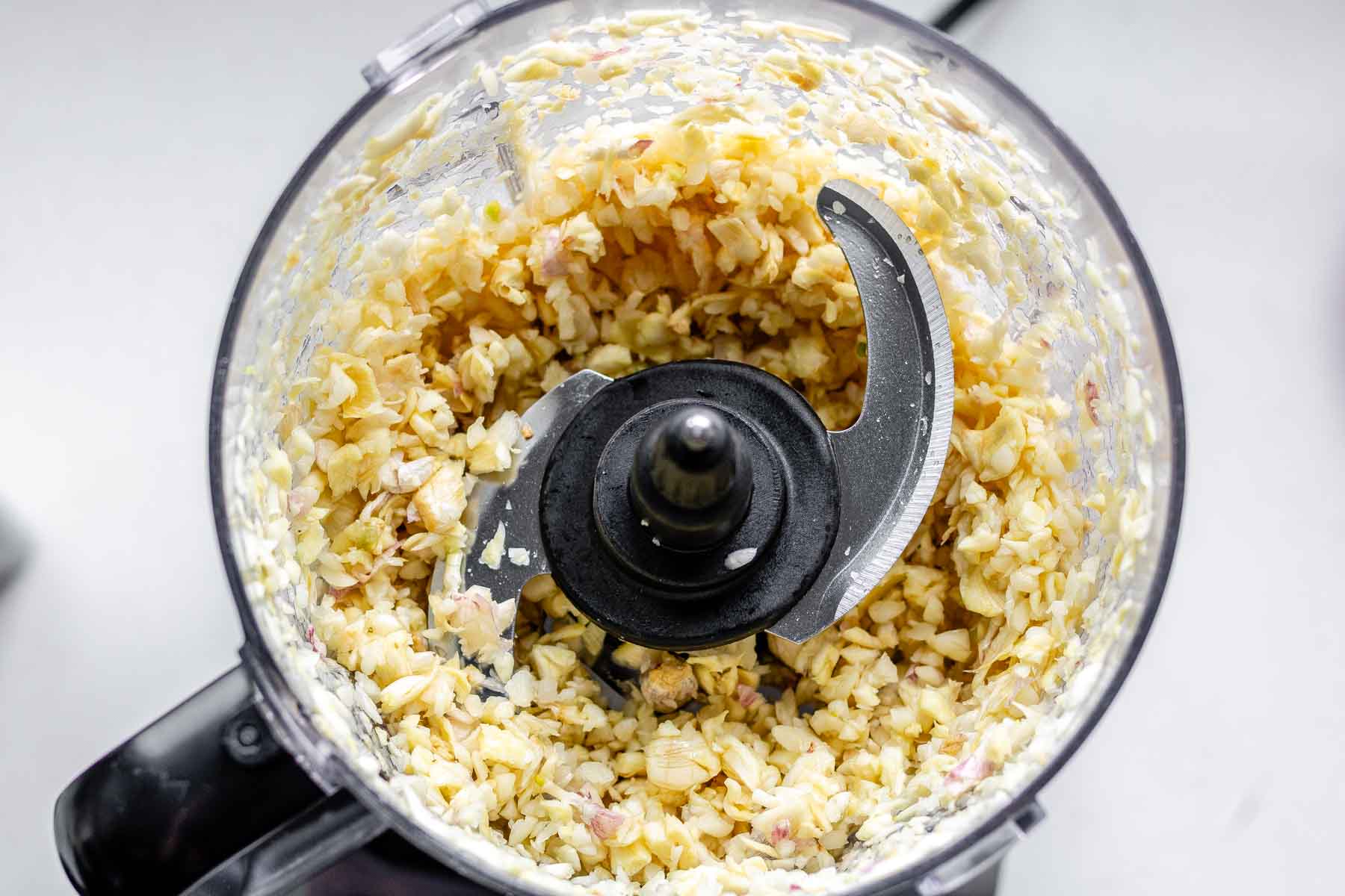 Processed garlic cloves in a food processor jar.
