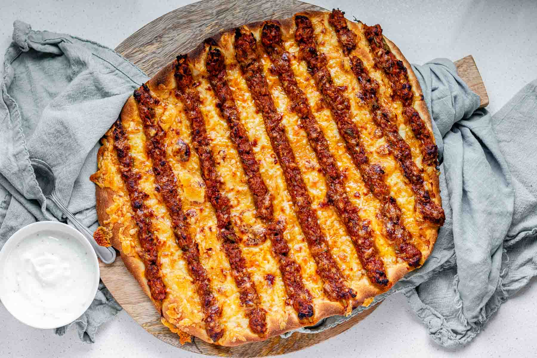 Flatbread topped with lines of cooked meat and cheese.