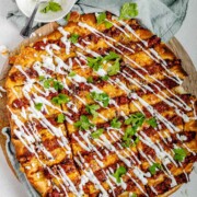 Flatbread topped with lines of cooked meat and cheese, drizzled with yogurt sauce, and scattered with cilantro leaves.