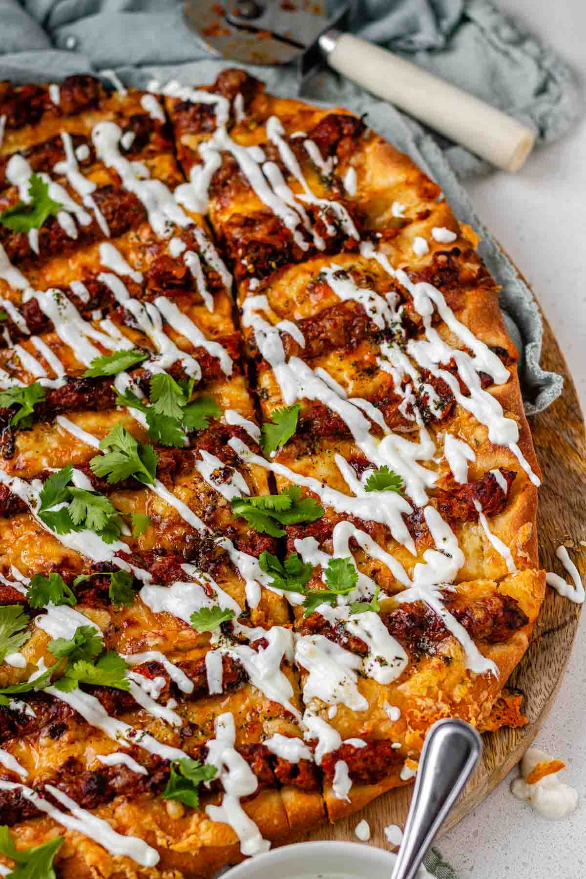 Flatbread topped with lines of cooked meat and cheese, drizzled with yogurt sauce, and scattered with cilantro leaves.
