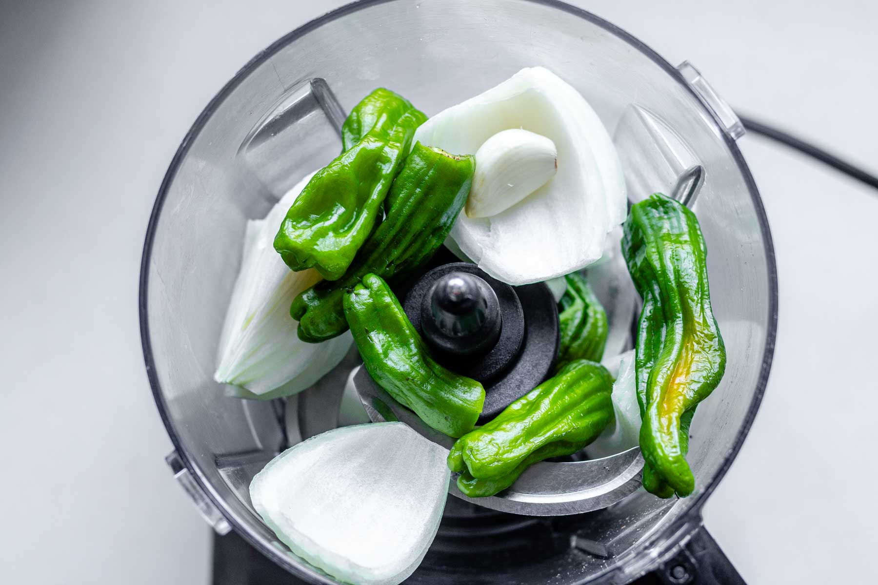 A food processor jar with onion, garlic and green peppers in it.