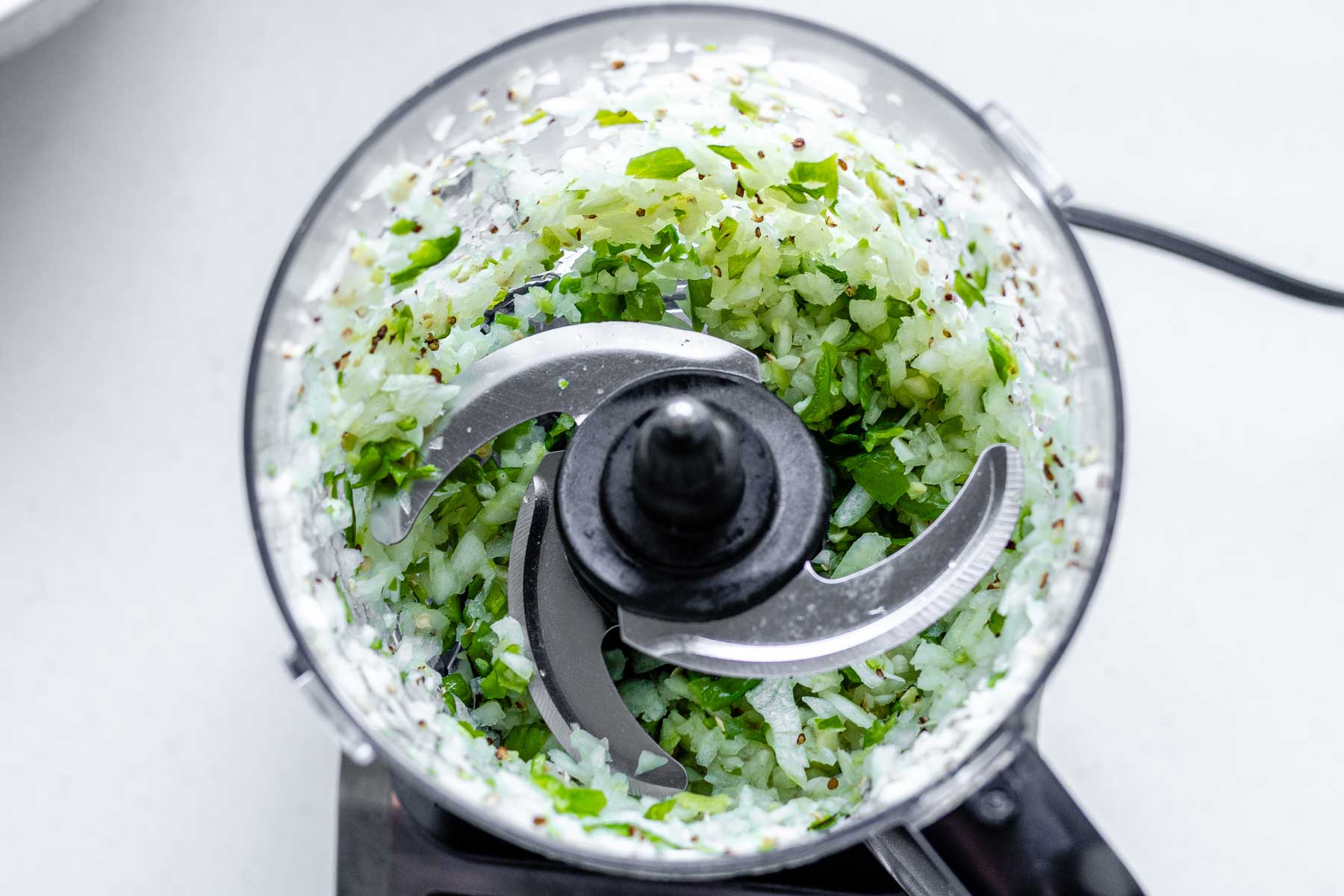 A food processor jar with blended onion, garlic and green peppers in it.