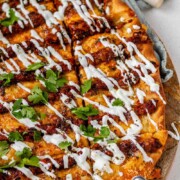 Flatbread topped with lines of cooked meat and cheese, drizzled with yogurt sauce, and scattered with cilantro leaves with the words lahmacun pide.