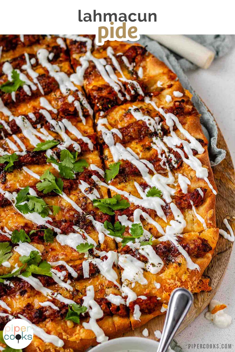 Flatbread topped with lines of cooked meat and cheese, drizzled with yogurt sauce, and scattered with cilantro leaves with the words lahmacun pide.