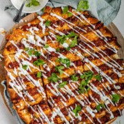 Flatbread topped with lines of cooked meat and cheese, drizzled with yogurt sauce, and scattered with cilantro leaves with the words lahmacun pide.