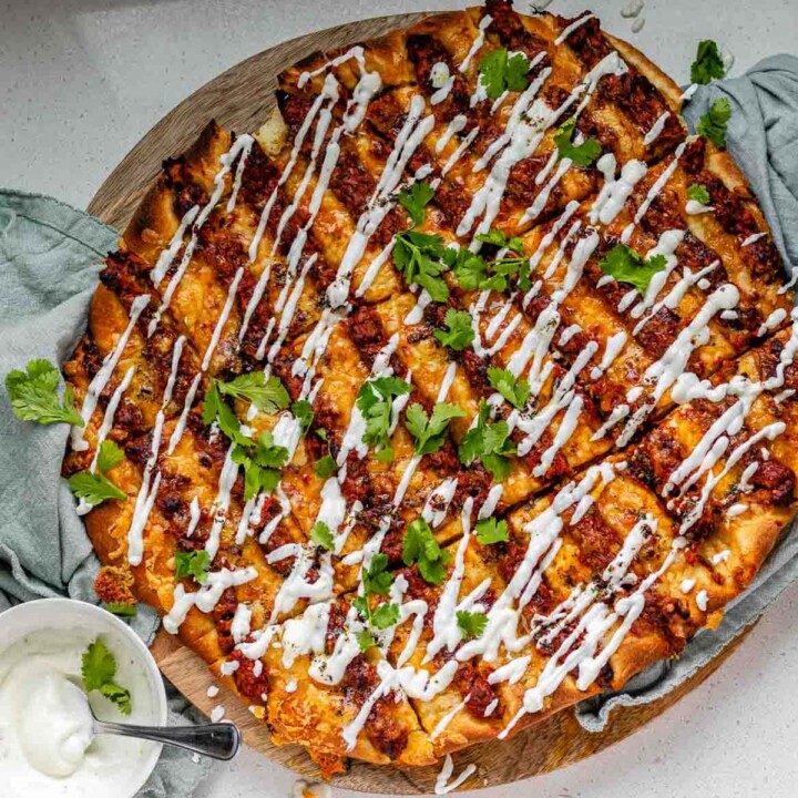 Flatbread topped with lines of cooked meat and cheese, drizzled with yogurt sauce, and scattered with cilantro leaves.