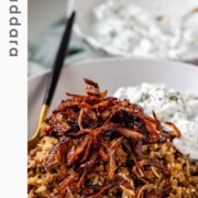 A bowl of rice and lentils, topped with crispy onions with the word mujaddara.