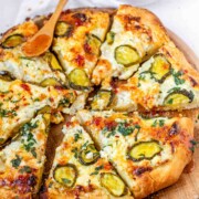 Pizza on a pizza peel topped with pickles and a red sauce.